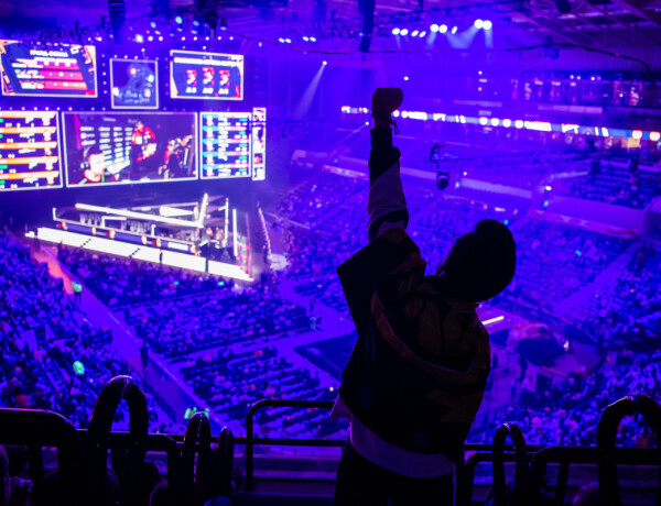 Big esports event. Video games fan on a tribune at tournament’s arena with hands raised. Cheering for his favorite team.